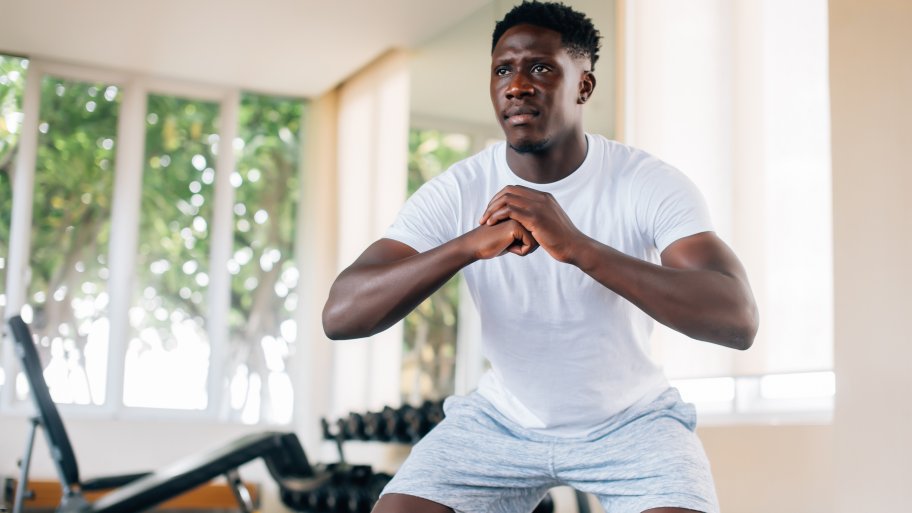 An African American man in a white shirt doing squats in his home gym